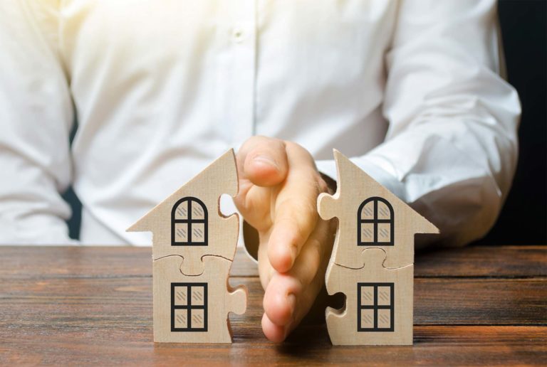 Hand teilt ein Haus in zwei Hälften, als Symbol für den Verkauf einer Immobilie bei Scheidung
