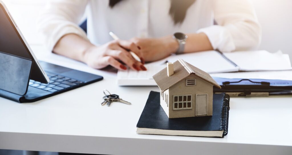 Unternehmerinnen, Geschäftsinhaberinnen, Buchhalterinnen und Immobilienmaklerinnen betrachten Modelle von Wohnhäusern auf dem Tisch, während sie mit Eigenkapitalrechnern ihr finanzielles Risiko bewerten.